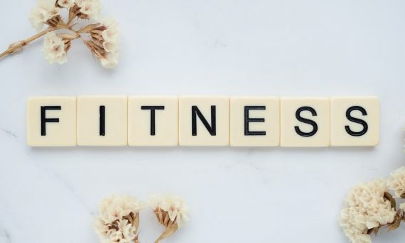 Close-up of scrabble tiles spelling 'FITNESS' on a marble surface with white flowers.