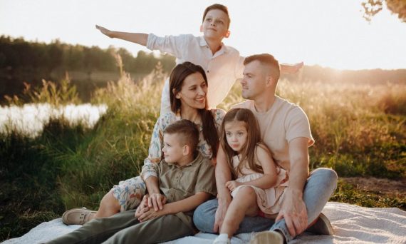 A family of five enjoying a serene picnic in a sunlit meadow during sunset.